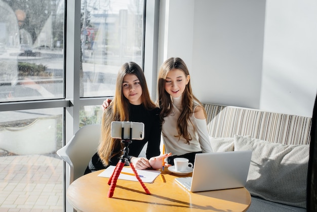 Two young beautiful girls are sitting in a cafe, recording video blogs and communicating on social networks.