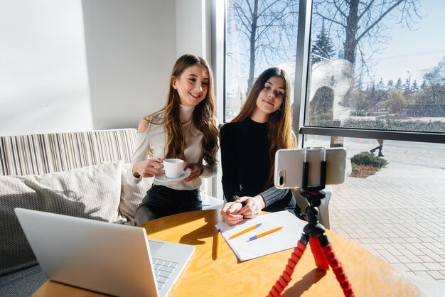 写真 2人の若い美しい女の子がカフェに座って、ビデオブログを録画し、ソーシャルネットワークで通信しています。