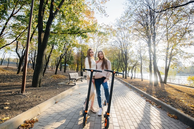 Two young beautiful girls ride electric scooters in the Park on a warm autumn day.