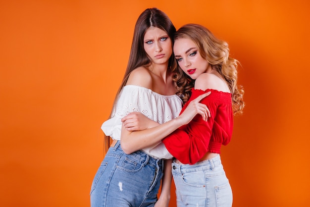 Due ragazze giovani e belle mostra emozioni e sorrisi su una parete arancione. ragazze per la pubblicità.