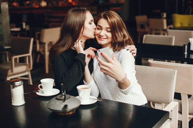 two young and beautiful girls sitting in a cafe and drinking a coffee