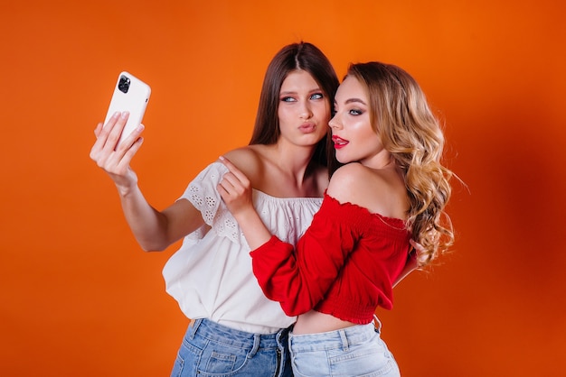 Two young and beautiful girls take a selfie and watch the phone in the Studio on a purple background. Girls for advertising.
