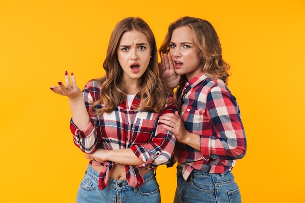 two young beautiful girls wearing plaid shirt frowning and expressing outrage isolated