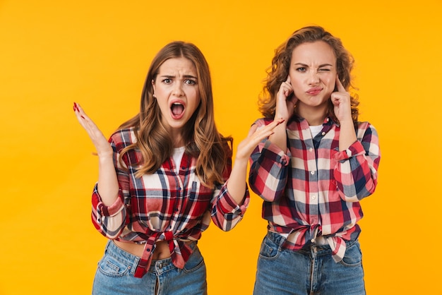 two young beautiful girls wearing plaid shirt screaming and having fight isolated