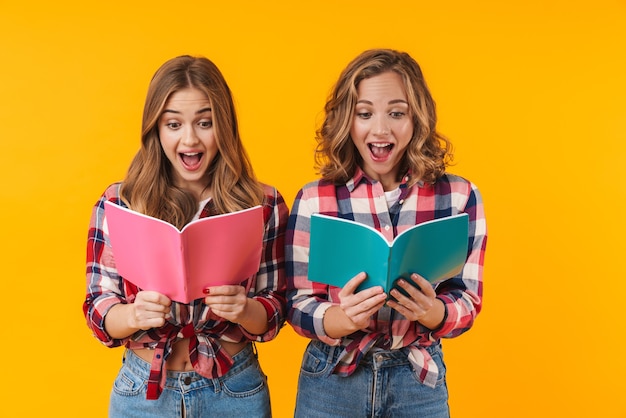 Two young beautiful girls wearing plaid shirts smiling and holding diary books isolated