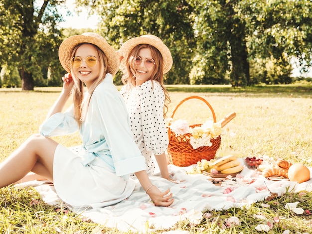 Due giovani belle donne sorridenti in prendisole e cappelli estivi alla moda. donne spensierate che fanno picnic all'esterno.