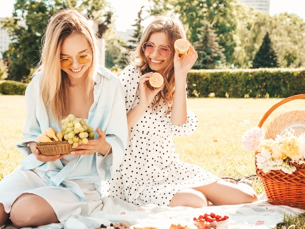 トレンディな夏のサンドレスと帽子の2人の若い美しい笑顔の女性。外でピクニックをするのんきな女性。