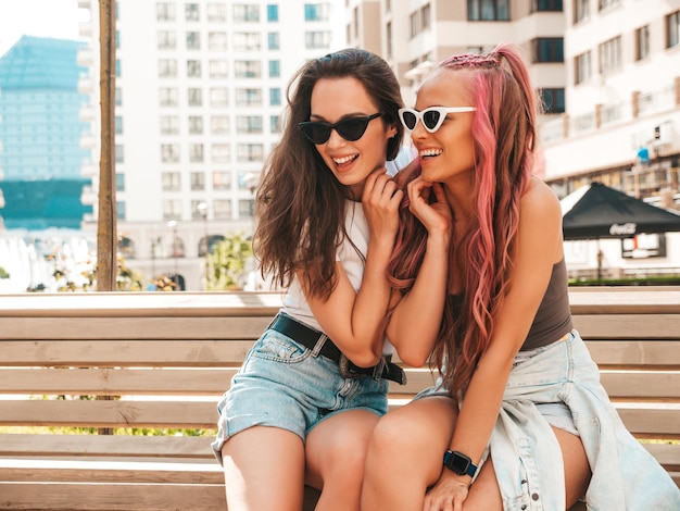 Two young beautiful smiling hipster female in trendy summer clothes.Sexy carefree women posing in the street with pink hair. Positive pure models having fun at sunset. Cheerful and happy