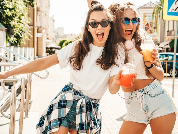 Two young beautiful smiling hipster female in trendy summer clothes