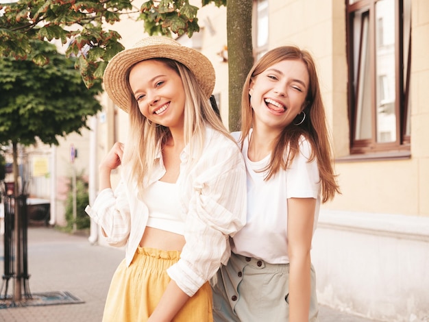 Two young beautiful smiling hipster female in trendy summer clothesSexy carefree women posing in the street in hat Positive pure models having fun at sunset