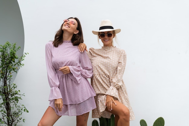 Two young beautiful smiling hipster female in trendy summer sundressSexy carefree women posing on the street background Positive models having fun