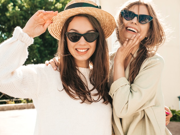 Two young beautiful smiling hipster female in trendy white sweater and coat