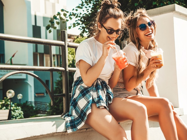 Two young beautiful smiling hipster girls in trendy summer clothes