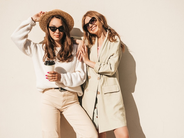 Two young beautiful smiling hipster girls in trendy white sweater and coat