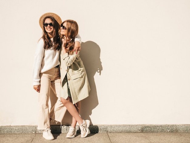Two young beautiful smiling hipster girls in trendy white sweater and coat