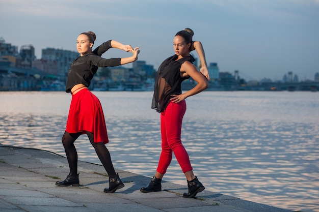 Due giovani belle sorelle gemelle stanno ballando una danza waacking sullo sfondo della città vicino al fiume