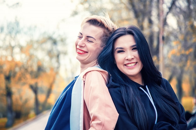 アジアとヨーロッパの2人の若い美しい女性は、夕日、友情の日の概念で背中合わせに立つ