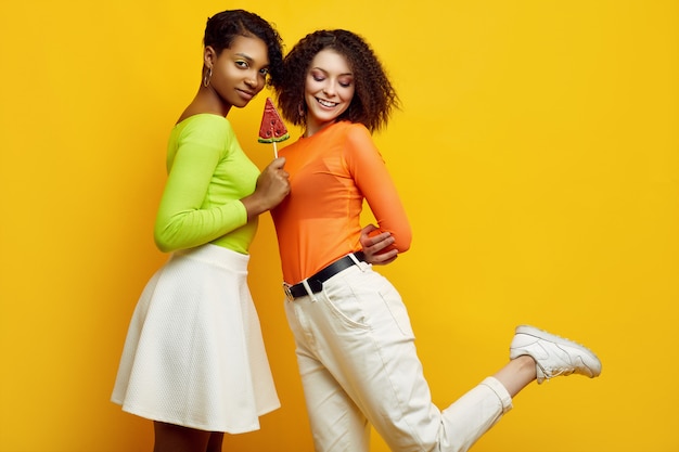 Two young beautiful women in colorful summer clothes with lollipops