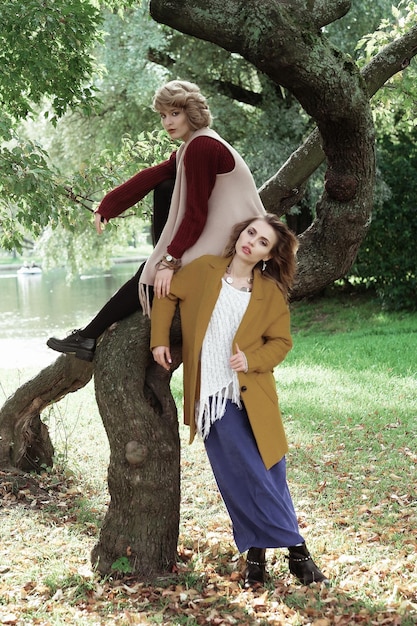 Two young beautiful women posing on a tree autumn park