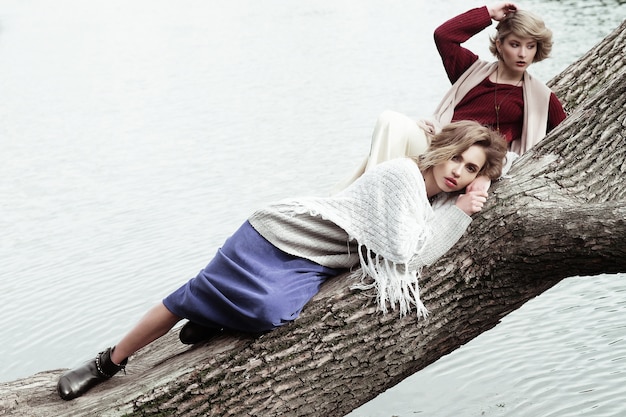 Two young beautiful women posing on a tree.