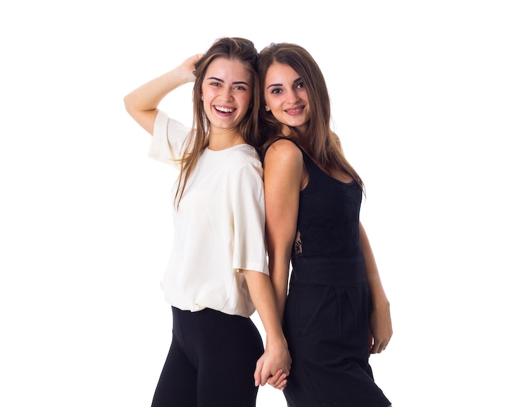 Photo two young beautiful women in white and black shirts holding hands on white background in studio