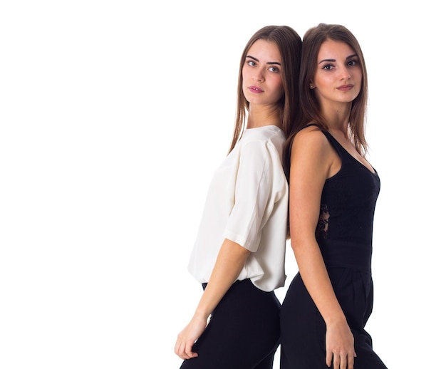 Two young beautiful women in white and black shirts standing back to back on white background