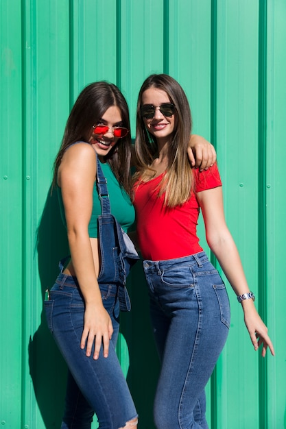 Two young best female friends standing by the green wall