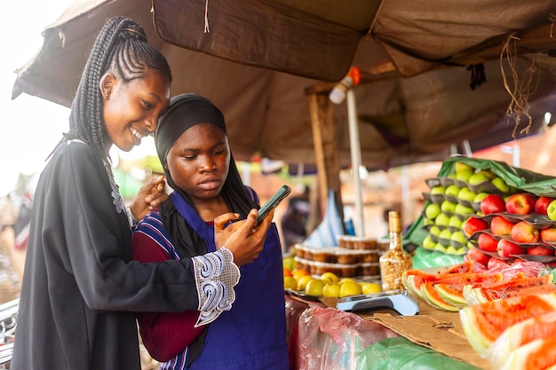 Two young black Women Looking at a Cell Phone in a Market