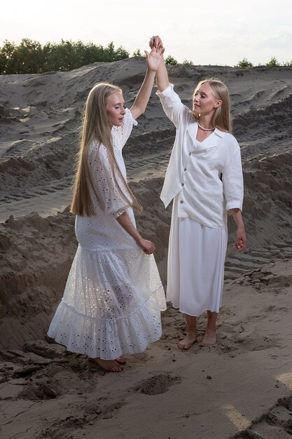 Two young blond pretty twins dancing at sand quarry in elegant white dress, skirt, jacket.