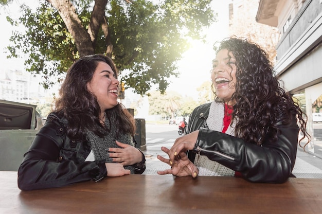 Photo two young brunette latina girls in black jackets and scarves laughing and chatting with each other