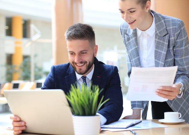 Two young business people using laptop in office while collaborating on startup project.