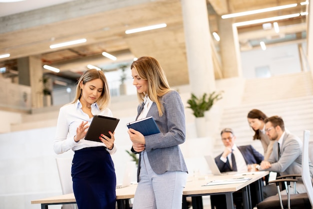 Two young business women looking at financial results on digital tablet in front of their team at the office