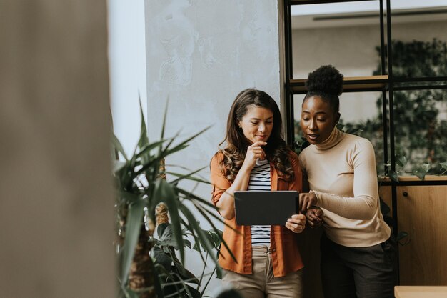 写真 現代のオフィスに立っているデジタルタブレットを持つ2人の若いビジネス女性