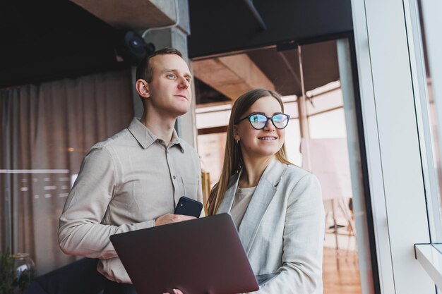 Two young businessmen and businesswomen smiling while sitting in the office talking and surfing the internet together with a laptop