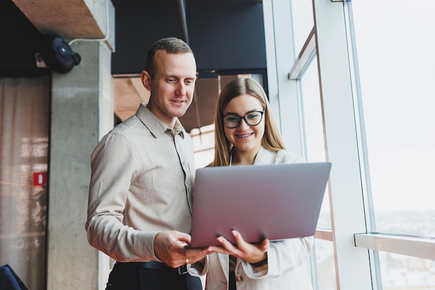 Two young businessmen and businesswomen smiling while sitting in the office talking and surfing the internet together with a laptop