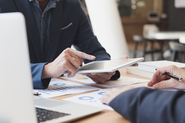 Two young businessmen using touchpad and analysis business chart document at meeting