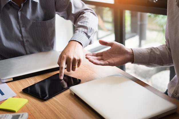 Two young businessmen using touchpad explaining his business plans to his colleagues, organization meeting concept