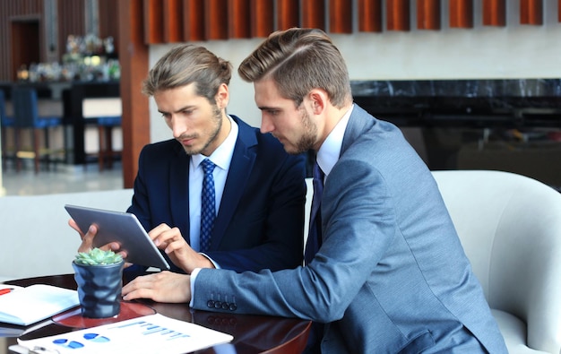 Two young businessmen using touchpad at meeting.