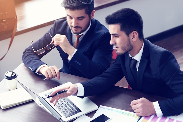 Two young businessmen working on laptop at  modern office. Beard hipster businessmen. Film effect, lens flare