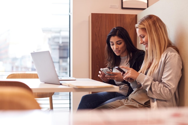 Two Young Businesswomen In Meeting Around Table In Modern Open Plan Workspace