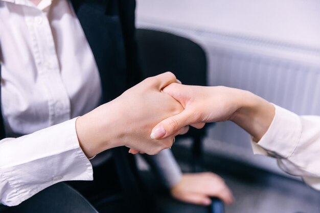 Two young businesswomen shake hands at the office celebrating v