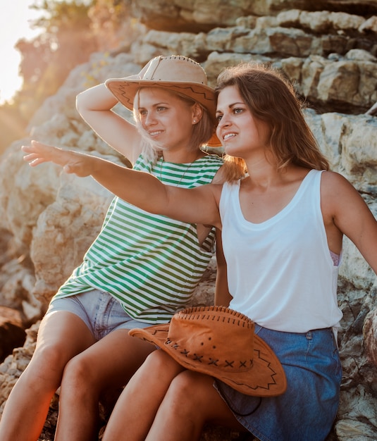 Two young cheerful women hipsters hats on  rock on the coast of the sea. 