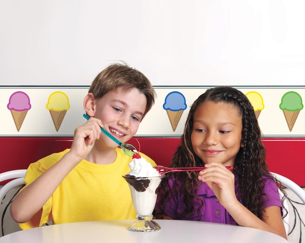 Two young children sharing a hot fudge sundae in an Ice Cream Shop