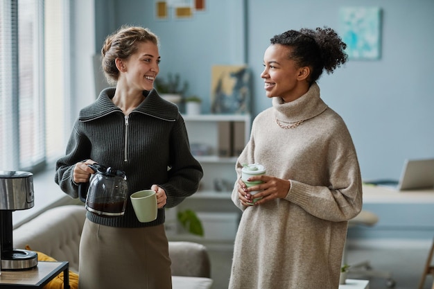 Two young colleagues drinking coffee together during break at office