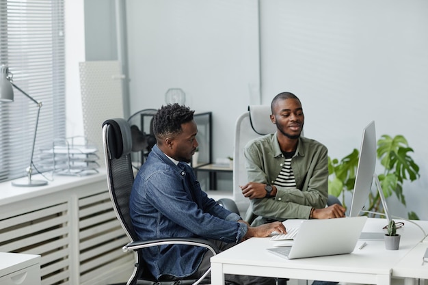 Two young confident programmers sitting by desk in front of computer monitor