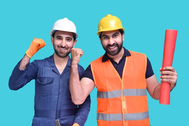 two young construction workers smiling over blue background indian pakistani model