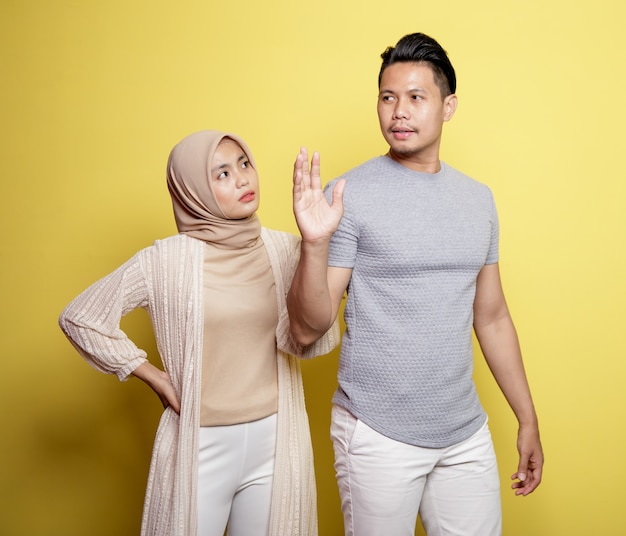 Two young couples wearing hijab and a man with an expression telling something to the woman isolated on yellow background