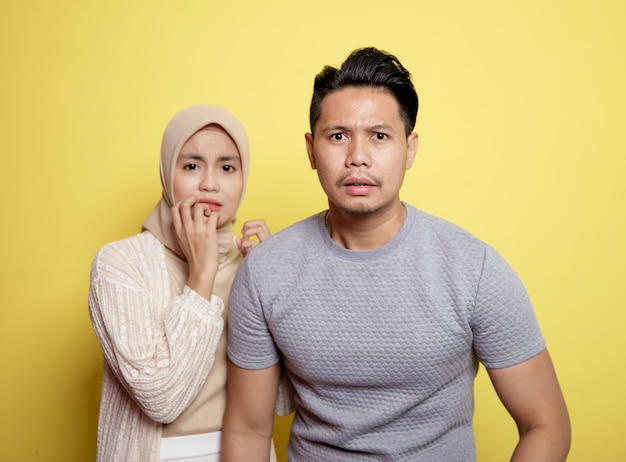 Two young couples a woman wearing hijab and a man with an expression scared looking at camera isolated on yellow background