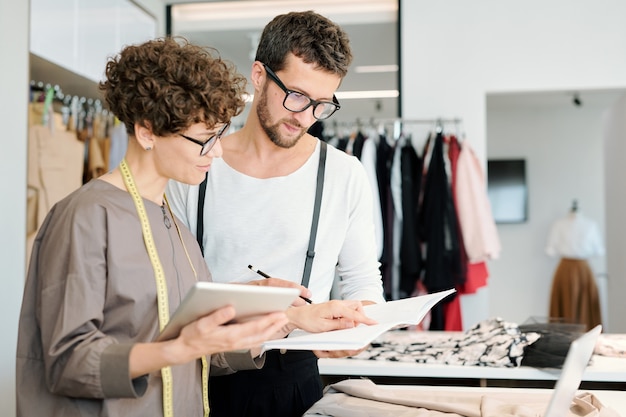 Two young creative fashion designers looking at new sketch for seasonal collection and discussing it