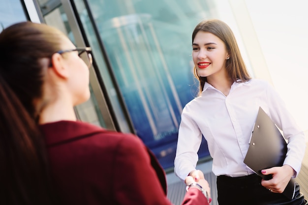 2人の若いかわいいビジネス女性が握手します。成功したトランザクション、契約、契約、ビジネス。